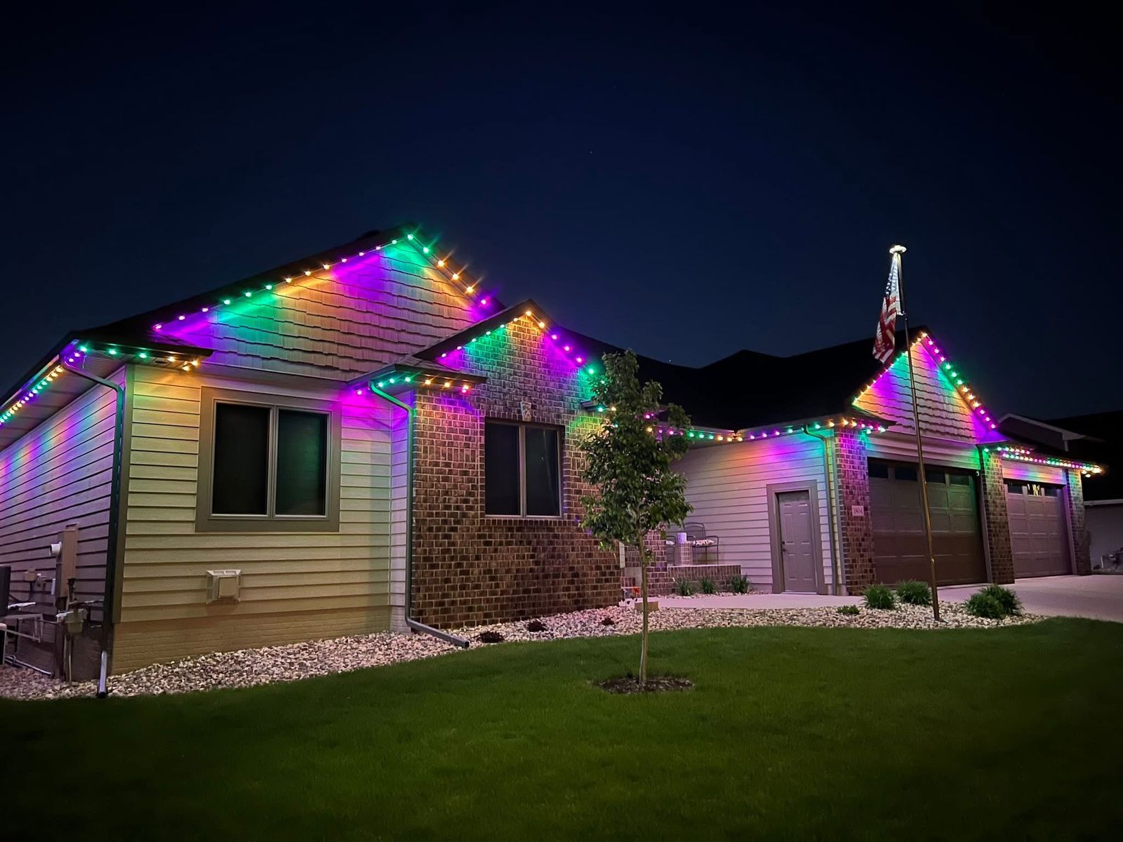 Permanent multicolor roofline lighting on a ranch home with American flag